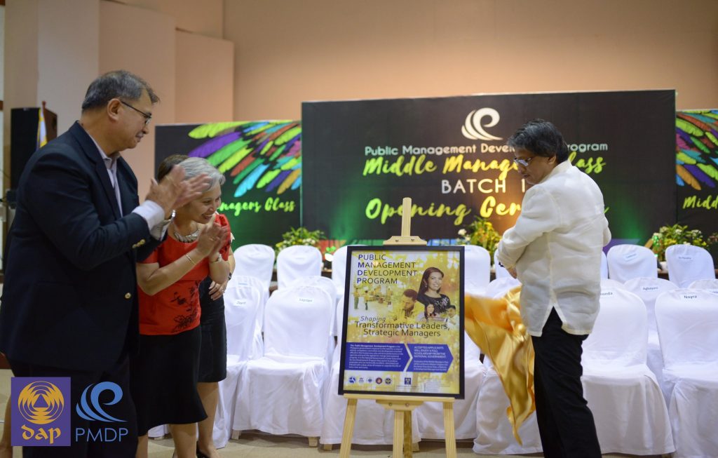 New poster.  DAP President Tony Kalaw Jr., SVP for Programs Dedeng Mendoza and PMDP  Director Nanette Caparros (partly hidden) admire a sample of the PMDP poster launched at the end of the opening ceremony for Batch 12 as Fortunato “Boy” de la Peña (left), lead  faculty of the program, applauds.  (Liz Ranola) 
